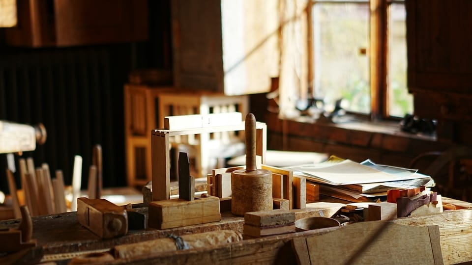 A cluttered wooden workbench in warm window light, with a mallet, hand planes and half-finished dovetailed frames.